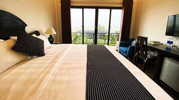 A hotel room with a large bed, a desk with a TV, and a balcony with a view.
