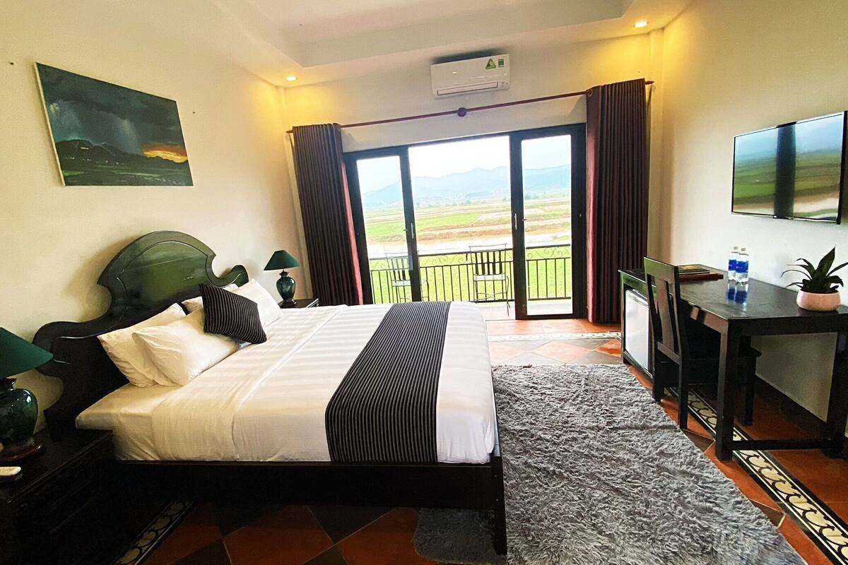 Habitación de hotel con cama, escritorio, televisor, balcón con vistas y aire acondicionado.