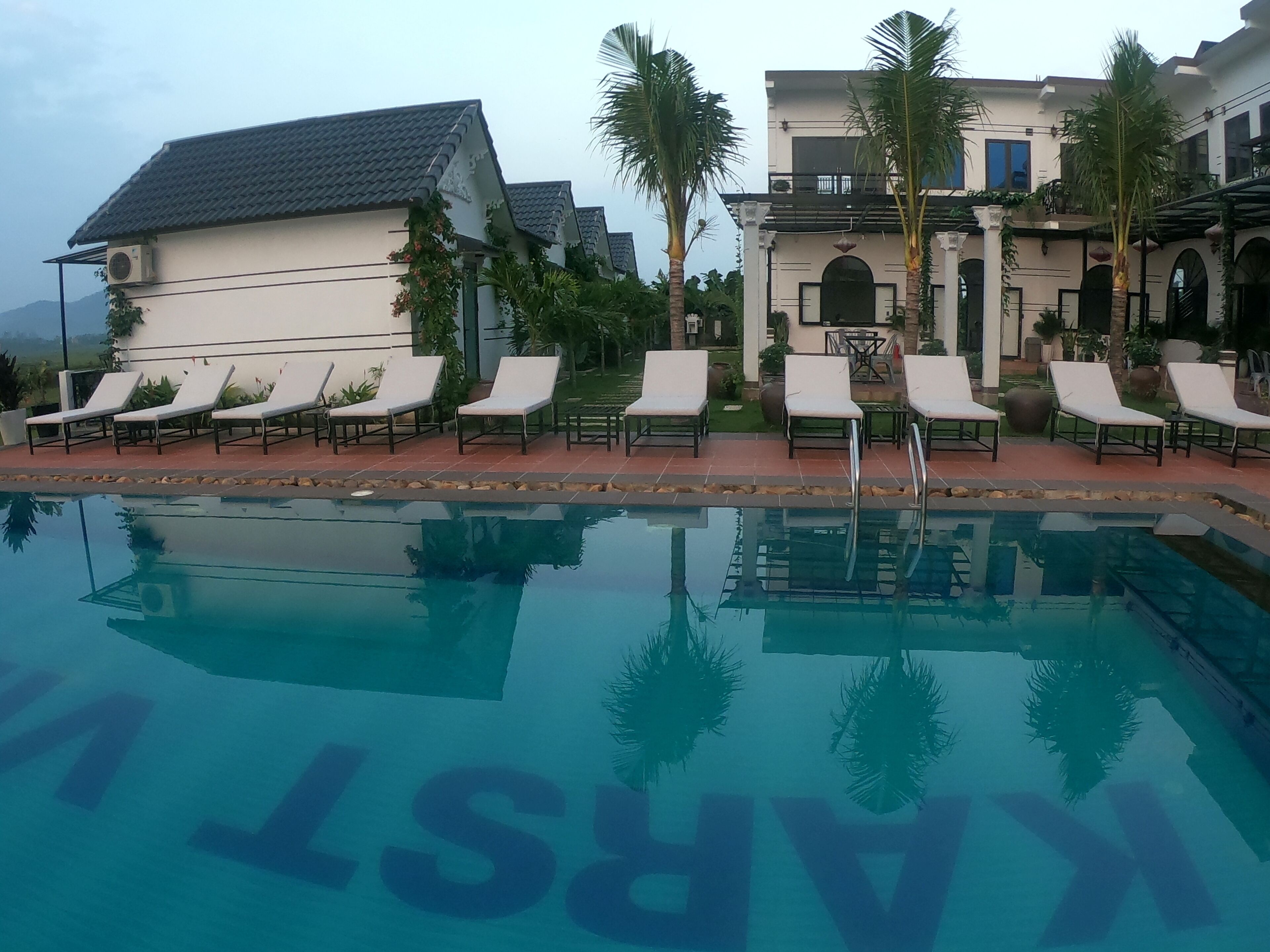 A swimming pool with lounge chairs and a building with a tiled roof and arched windows.