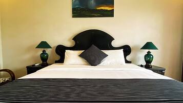 A neatly made bed with a striped bedspread, two green lamps on nightstands, a black headboard, and a painting of a stormy landscape on the wall.