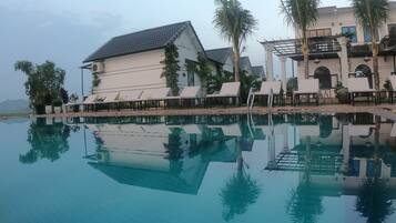 A poolside area with lounge chairs, a building with a tiled roof, and palm trees.