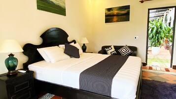 A neatly made bed with a black headboard, white bedding, and striped throw. There are two bedside tables with lamps, a small nightstand, and a decorative rug.