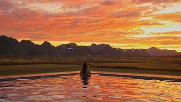 Una persona en una piscina con vista al atardecer y montañas.