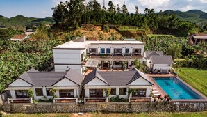 A large, multi-story building with a swimming pool, surrounded by lush greenery and hills.