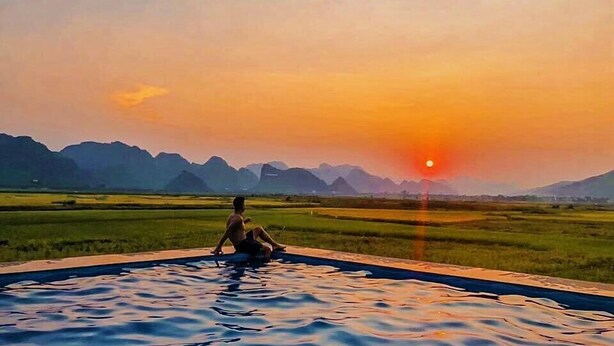 A person sitting by a pool with a sunset and mountains in the background.