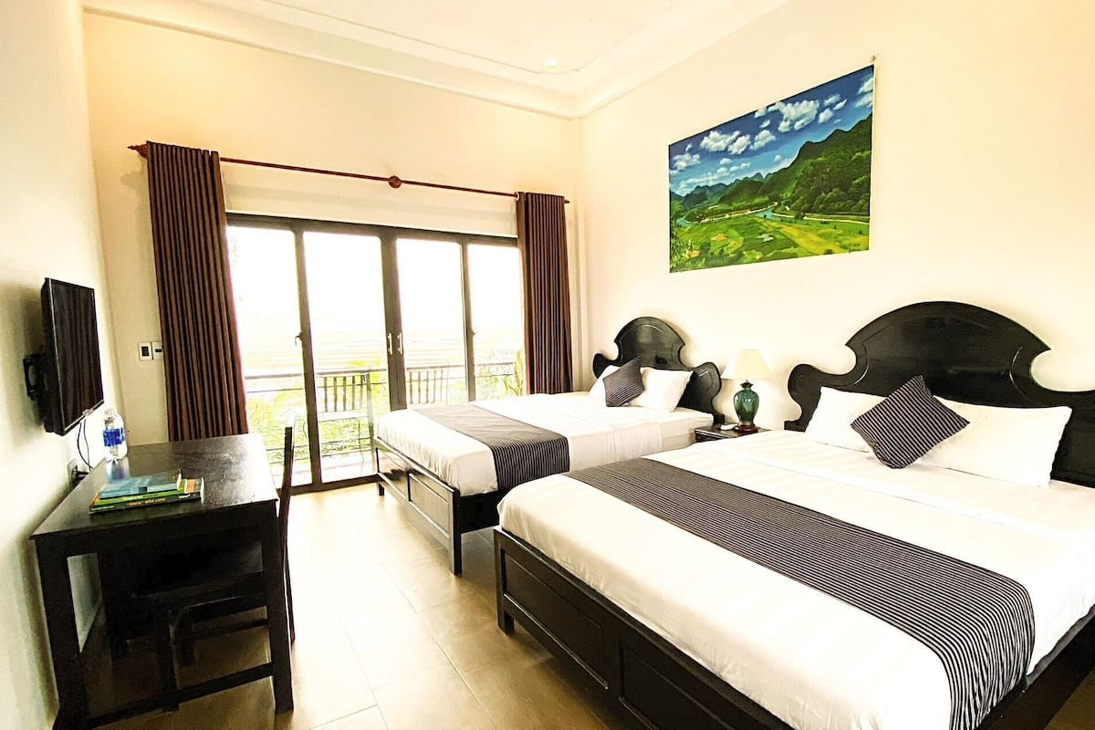 Habitación de hotel con dos camas, un escritorio, un televisor, un cuadro y vistas a un paisaje verde.