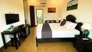 A hotel room with a bed, a desk with a TV, a lamp, and a painting on the wall.