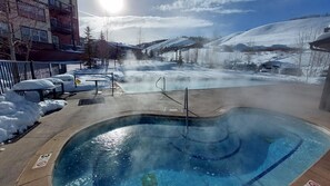 A hot tub with a view of a snowy mountain landscape, a fenced area with benches, and a building in the background. - Granby Ranch Ski Condo with King Bed & Bunkbed! (Granby)