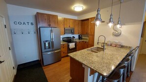 A modern kitchen with stainless steel appliances, wooden cabinets, granite countertops, and pendant lighting. - Granby Ranch Ski Condo with King Bed & Bunkbed! (Granby)