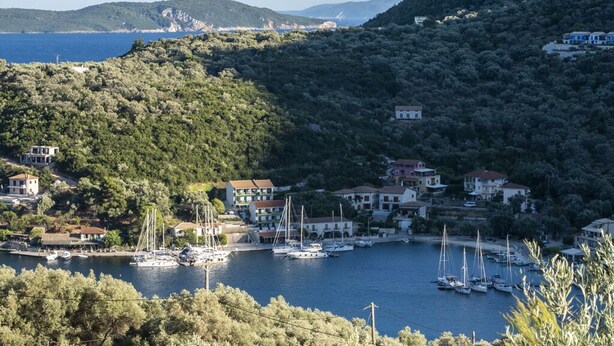 Un village côtier avec des maisons et des bateaux amarrés dans une marina, entouré de collines et offrant une vue dégagée sur la mer.