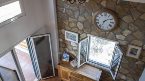 Une pièce avec un mur en pierre, une horloge, un banc en bois et une grande fenêtre.