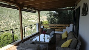 Un espace extérieur aménagé, abrité et doté de mobilier en osier, d’une table en verre et offrant une vue sur le paysage environnant.