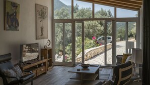 Un salon équipé d’un téléviseur, de sièges et offrant une vue sur un jardin et des montagnes.