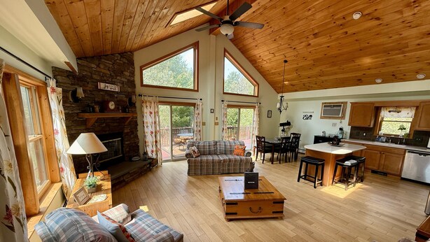 A spacious living room with a fireplace, a cozy seating area, a kitchen with a bar, and large windows offering a view of the outdoors. - Peaceful Catskill Mountains Cabin (Lexington)