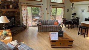 A spacious living room with a fireplace, a plaid sofa, a wooden coffee table, and a dining area with a table and chairs. - Peaceful Catskill Mountains Cabin (Lexington)