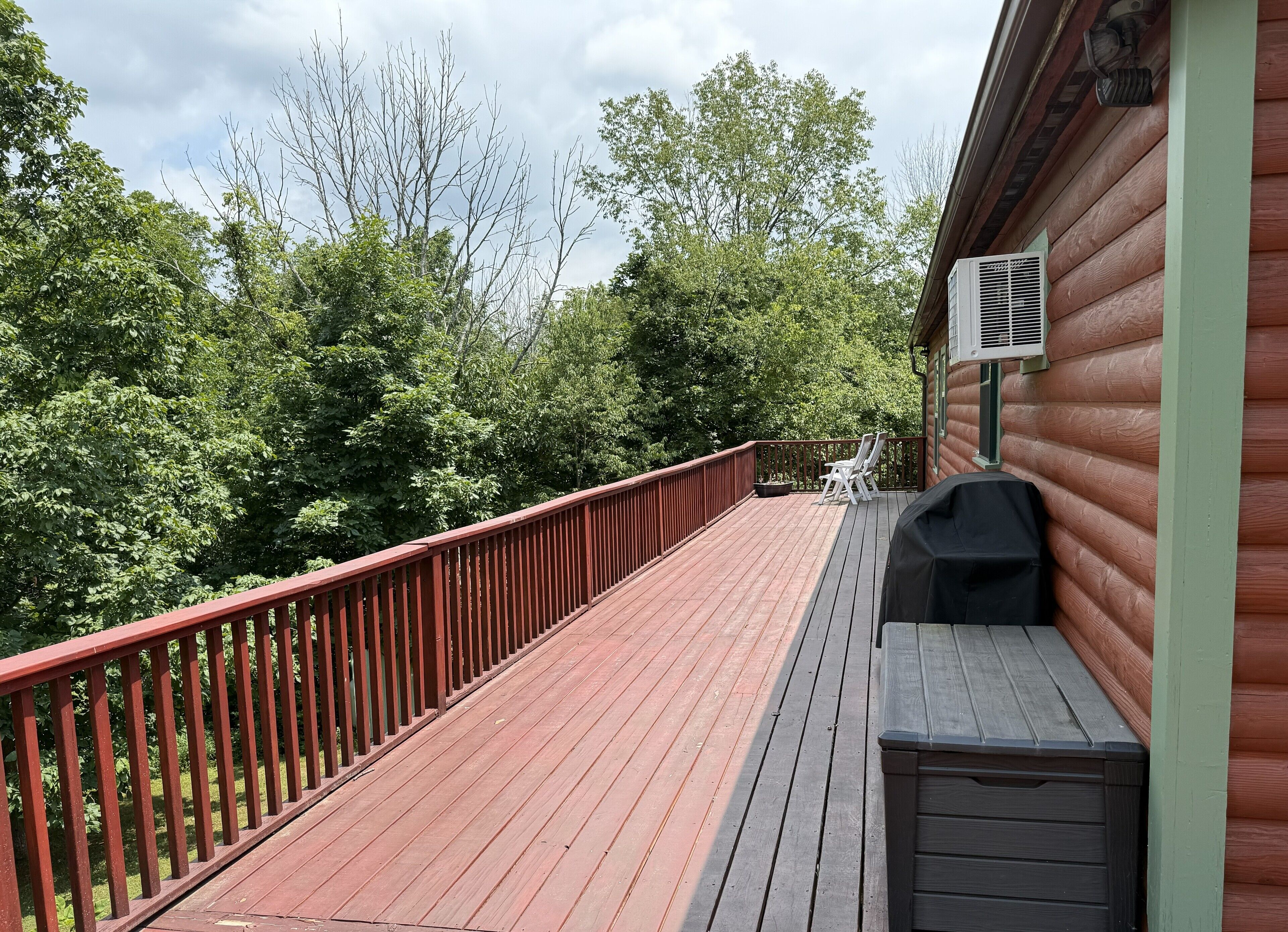 A wooden deck with a red railing, a barbecue grill, and a white outdoor chair.