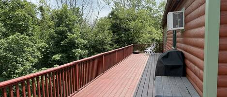 A wooden deck with a red railing, a barbecue grill, and a white outdoor chair.