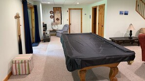 A room with a pool table, a chair, a small table with a lamp, a striped ottoman, and a birdcage. - Peaceful Catskill Mountains Cabin (Lexington)