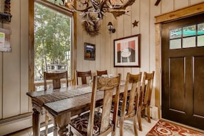 Un comedor con una mesa y sillas de madera, una araña y un cuadro en la pared.