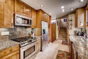 Una cocina con armarios de madera, electrodomésticos de acero inoxidable, encimeras de granito y piso de baldosas.
