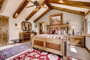 A bedroom with a wooden bed, a ceiling fan, a large mirror, and a window with a view. - Epic Lake and Mountain Views! (Dillon)