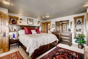 Une chambre à coucher avec un grand lit, une tête de lit en bois, des tables de chevet, une commode, un miroir et un tapis rouge.