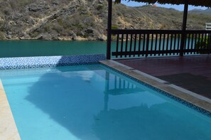 A swimming pool with a tiled edge, a wooden deck, and a view of a natural landscape.
