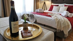 Une chambre d’hôtel avec un lit, une table de chevet sur laquelle se trouvent une bouteille de vin, des verres, un carnet et une plante en pot.
