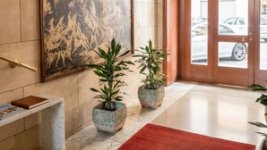 Un hall d’entrée agrémenté d’un grand tableau, de deux plantes en pot, d’un tapis rouge et d’un sol en marbre.