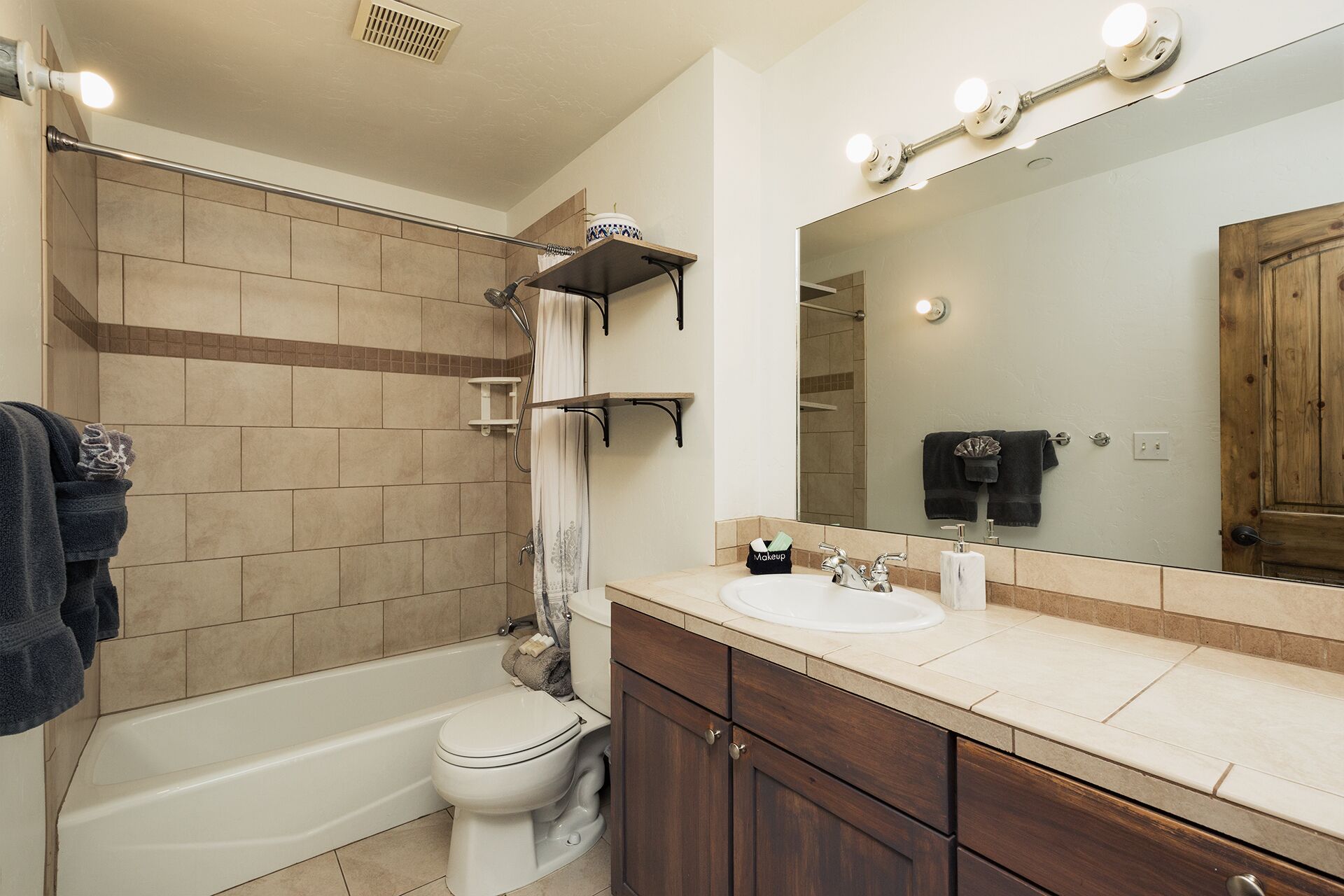 Une salle de bain équipée d’une baignoire, de toilettes, d’un meuble-lavabo avec un miroir et d’une étagère contenant des articles de toilette.