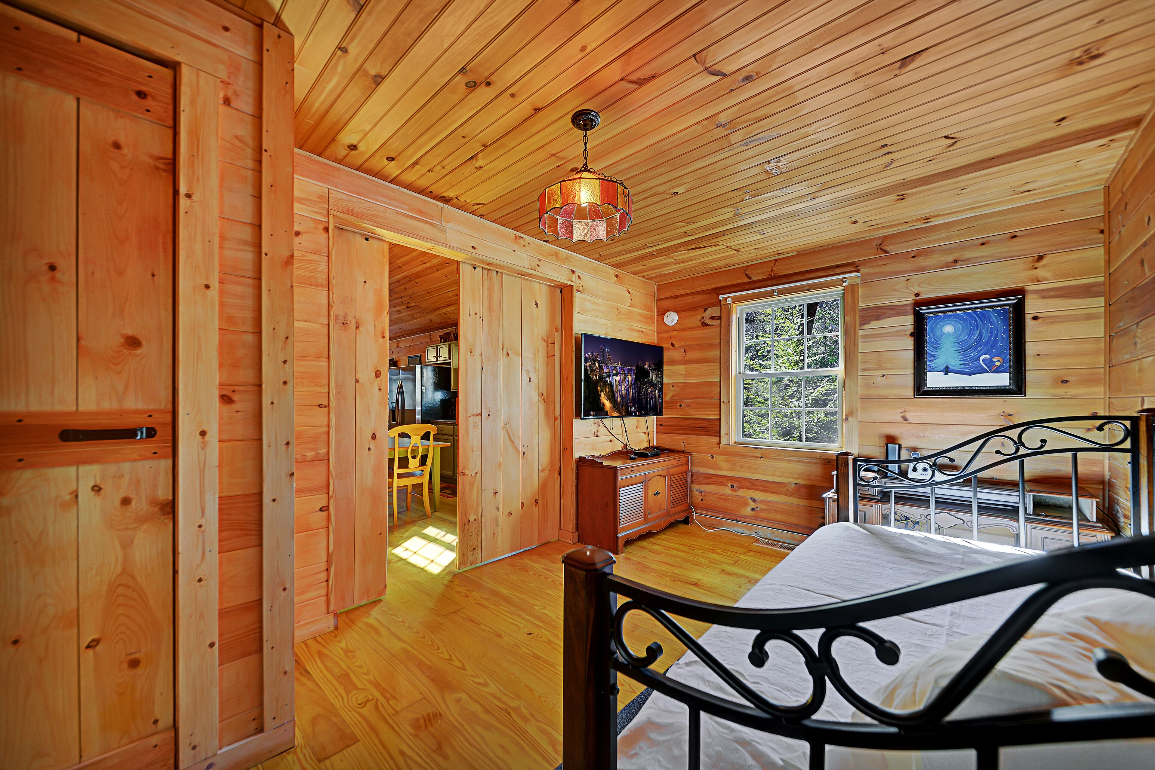A wooden cabin bedroom with a bed, a dresser, a television, and a window.