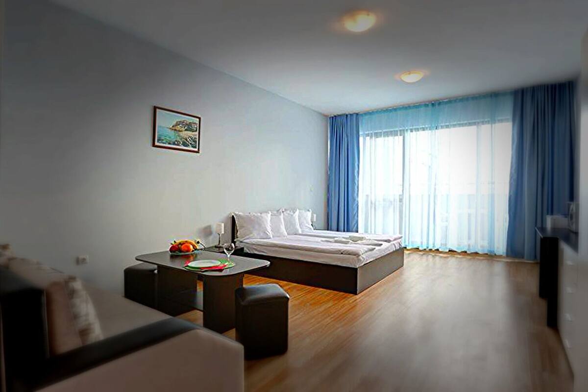 A modern hotel room with a large bed, a small table with fruits, a sofa, and a painting on the wall.