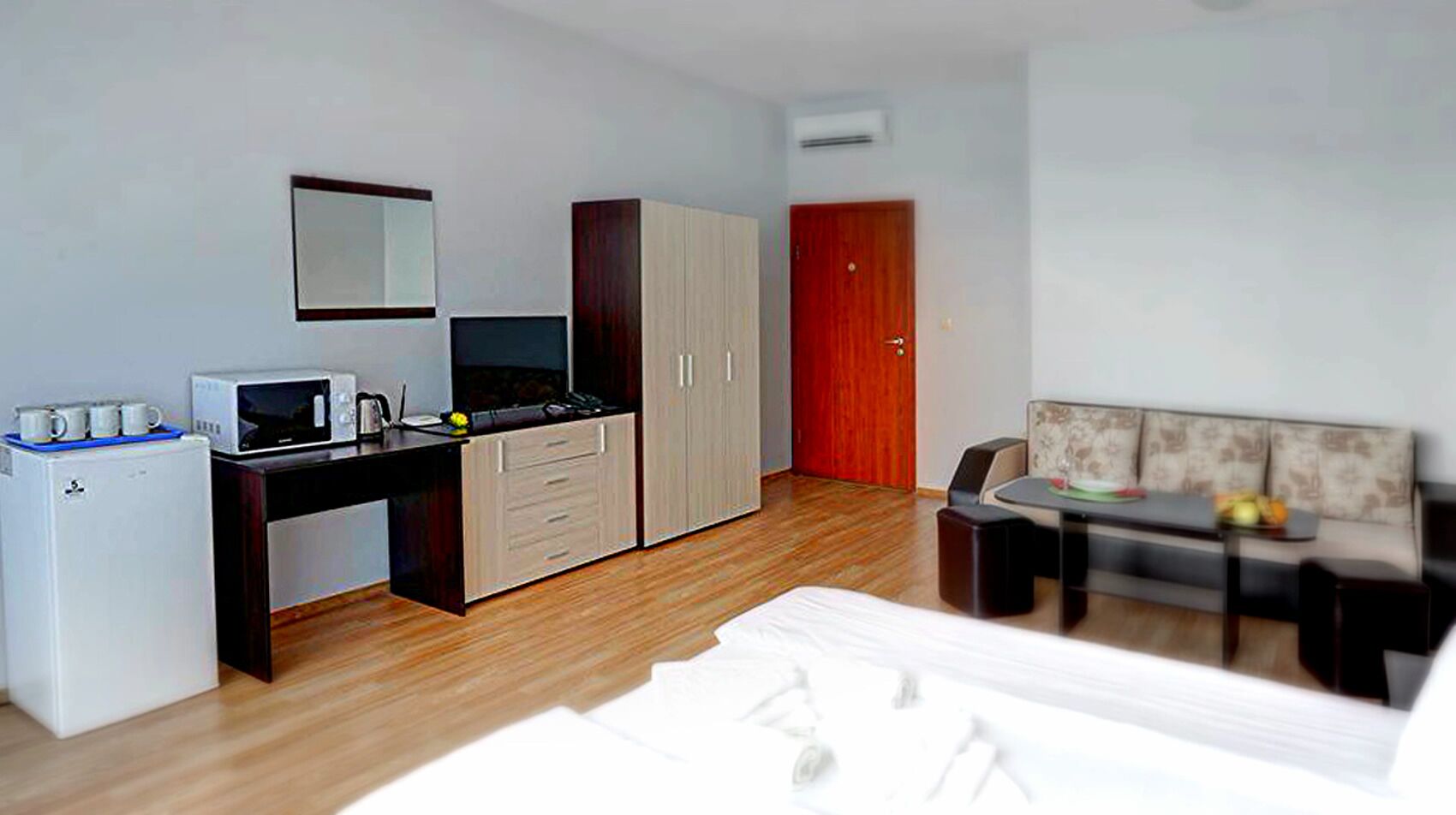A compact hotel room with a kitchenette, a bed, a sofa, and a dining table.