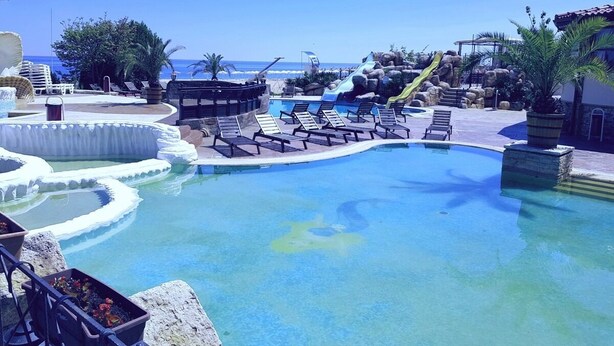 A resort pool with a water slide, lounge chairs, and a view of the ocean. - 1-st Line Izvora Hotel Golden Sands (Golden Sands)