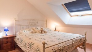 A bedroom with a bed, a nightstand, a lamp, and a skylight.
