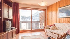 A cozy living room with a sofa, a television, and a view of snowy mountains through a large sliding glass door.