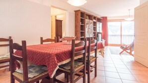 A dining area with a table set for four, wooden chairs, a cabinet with shelves, and a television.