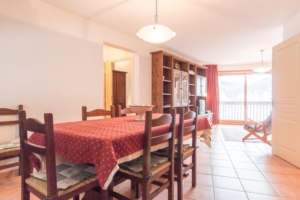 Een eethoek met een tafel voor vier personen, houten stoelen, een kast met planken en een televisie.