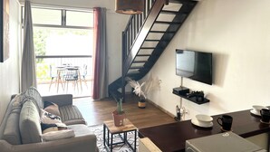 A living room with a sofa, coffee table, TV, and a staircase. - Cozy studio in Le Gosier 2 minutes from the beach (Le Gosier)