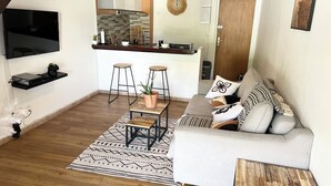 A living room with a sofa, a coffee table, a TV, and a kitchen area in the background. - Cozy studio in Le Gosier 2 minutes from the beach (Le Gosier)