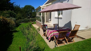 Une terrasse extérieure avec une table et des chaises, un grand parasol et une vue sur un bâtiment blanc doté de grandes fenêtres.