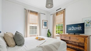 Un dormitorio con cama, cómoda de madera, televisor y ventana con cortinas.