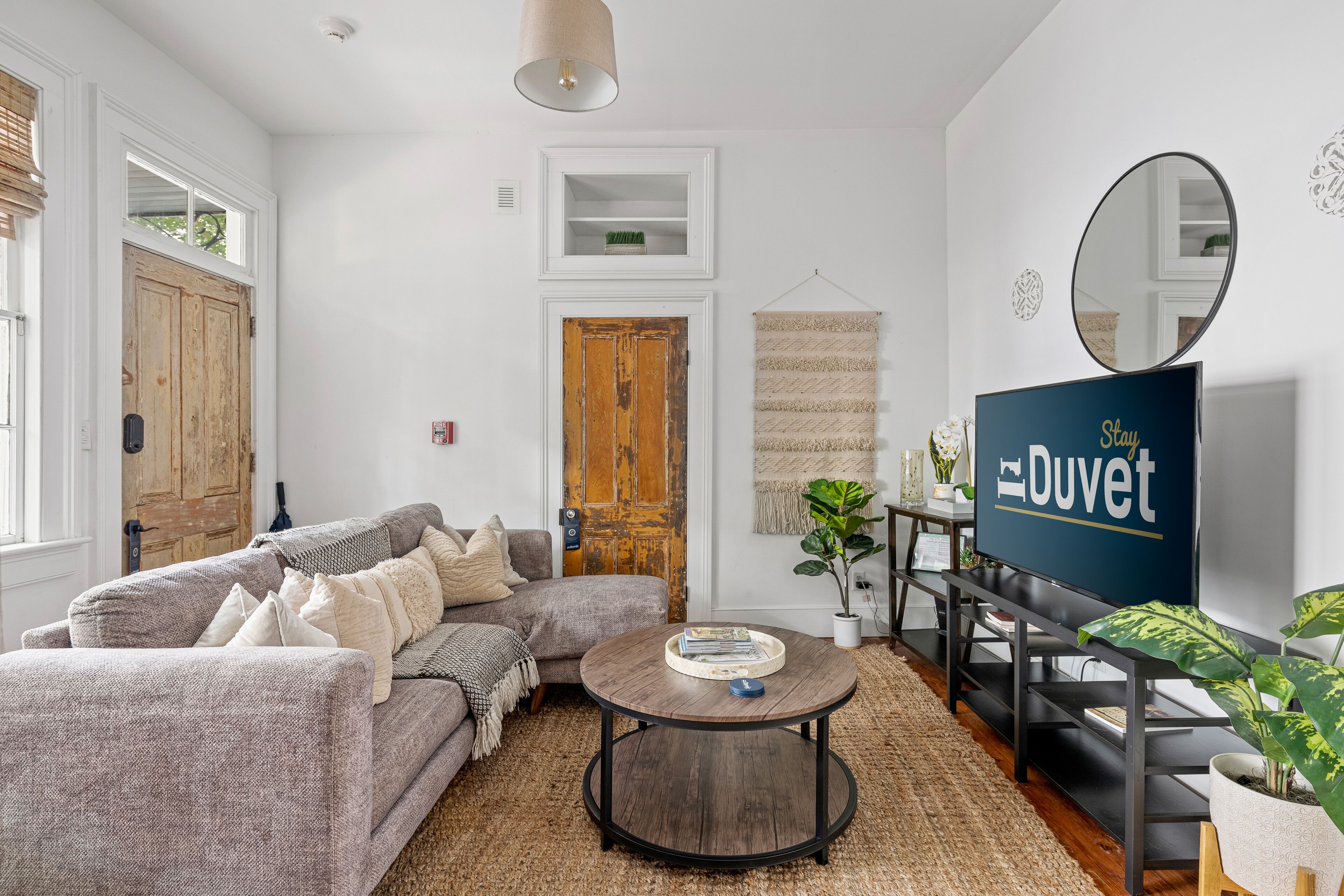 Ein Wohnzimmer mit grauem Sofa, Couchtisch, Fernseher und Holztür.