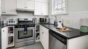 Una cocina moderna con armarios blancos, electrodomésticos de acero inoxidable, horno empotrado y lavavajillas.
