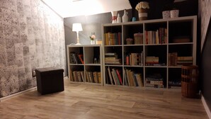 A room with a bookshelf filled with books, a small table with a lamp, and a trash bin. - Bluebell (Mengusovce)