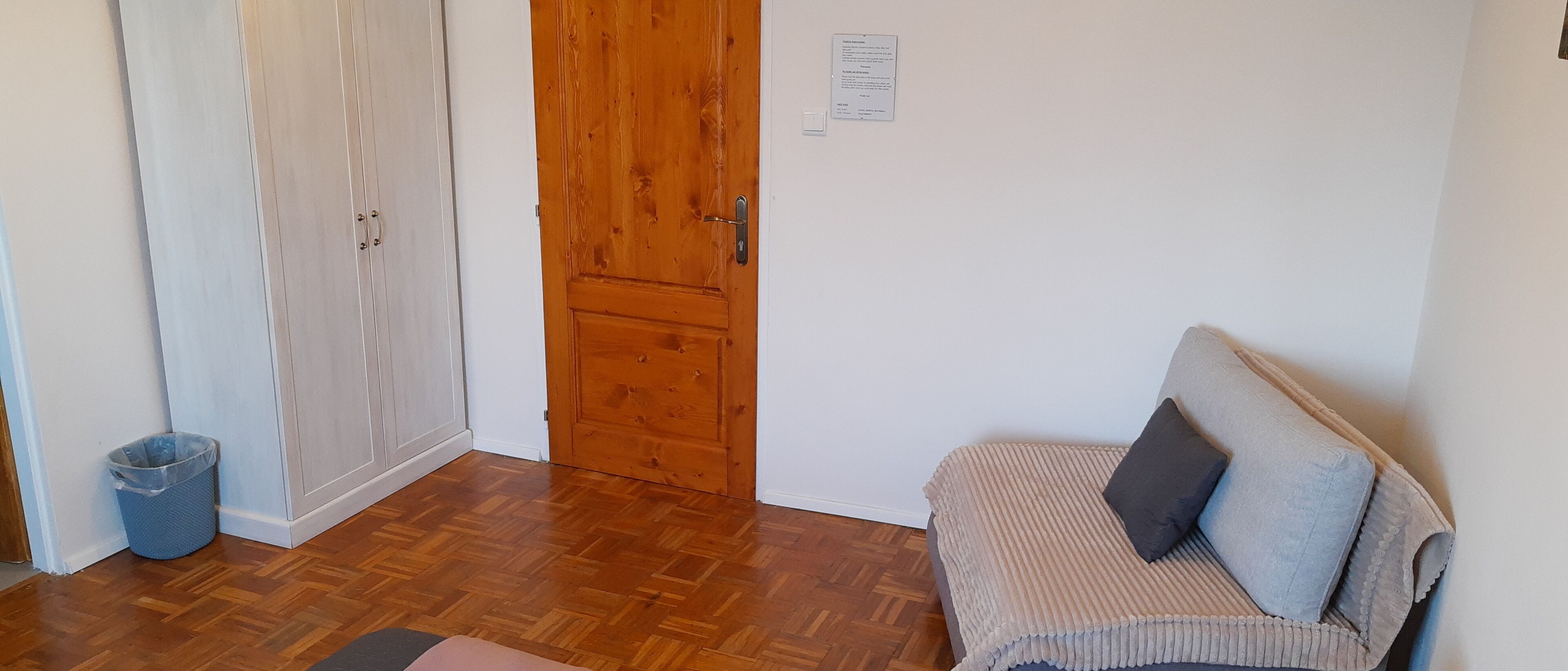 A room with a wooden door, a white wall, and a sofa with cushions.