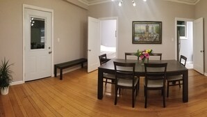 Een eetkamer met een ronde tafel, zes stoelen, een vaas met bloemen en een schilderij aan de muur.