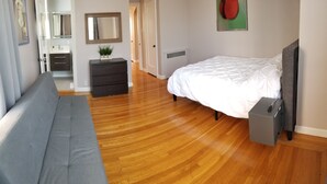 Une chambre à coucher avec un lit, un canapé gris, une commode, un miroir et un radiateur.