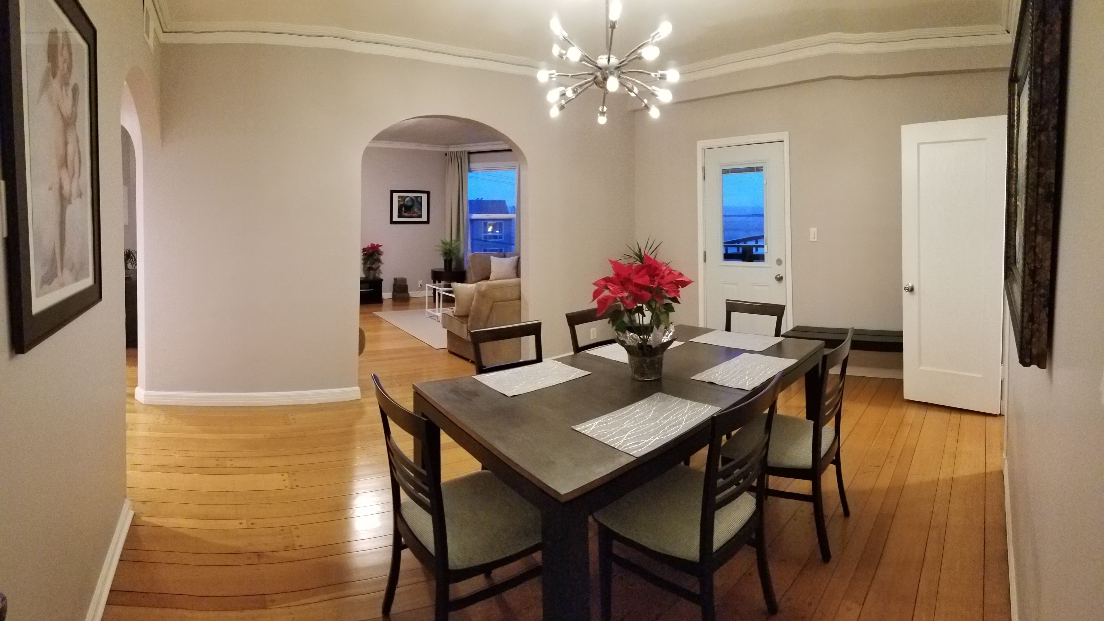 Uma sala de jantar com uma mesa posta para quatro pessoas, um candelabro e vista para outro espaço através de um arco.