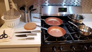 Een keuken met een fornuis, pannen, een snijplank en keukengerei.